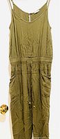 Front view of olive green romper hanging on hanger with visible zipper and drawstring waist showing pockets and adjustable thin shoulder straps.
