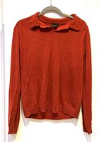 Front view of the bright terracotta silk sweater on a hanger, showing collar and long sleeves.