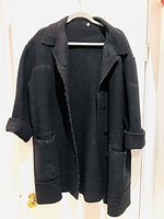 Front view of the black wool coat hanging on a hanger showing buttons, collar, and pockets.