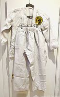 Full view of white youth karate gi jacket and pants hanging on hangers