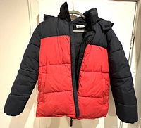 Front view of a color block navy blue and red youth winter jacket hanging on a door, showing the puffer/quilted design, zipper front, and pockets.