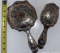 Both hand mirror and hairbrush shown together with measuring tape for size reference