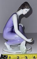 Side view of Hollohaza porcelain figurine showing woman crouching with purple dress, holding gold-accented object near base
