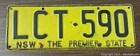 Yellow NSW license plate with black embossed registration number LCT-590 and inscription 'NSW THE PREMIER STATE'