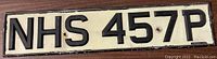 Front view of vintage license plate with black embossed text NHS 457P on white background.