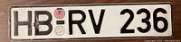 Front of the license plate showing embossed characters HB RV 236 with two official stickers.