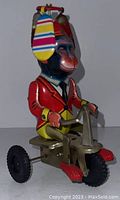 Side view of wind-up tin litho monkey toy riding a tricycle with colorful propeller on red helmet.
