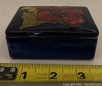 Side view of Moorcroft pottery box against measuring tape showing about 3 inch length.