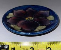 Side profile of Moorcroft pottery plate showing thickness and depth of floral design with measuring tape indicating diameter is about 6 inches.