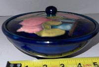 Side view of Moorcroft pottery covered dish showing floral embossed design and measurement tape indicating width.