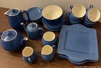 Full view of all dinnerware items arranged including coffee pot, tea pots, creamers, sugar bowl, plates, cups, saucers and bowl in powder blue glaze with white interiors.