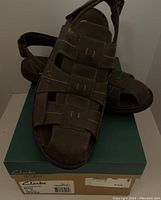 Pair of brown Clarks sandals on top of a Clarks shoebox, front and side view showing upper leather and Velcro straps.