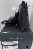 Pair of men's black Kenneth Cole dress shoes displayed on top of Kenneth Cole shoebox showing side and angled view.