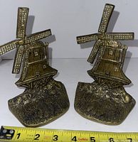 Pair of brass windmill shaped bookends with a measuring tape showing approximately 4.5 inches tall.