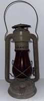 Full view of the vintage metal lantern with deep red glass globe and large carrying handle.