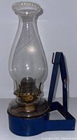 Full view of the vintage lantern showing glass chimney, metal burner, and blue metal base with handle.