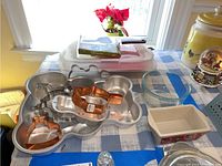 Overall view of bakeware set on table including metal molds, cookie cutters, plastic container, and other items