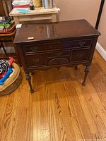 Front view of the vintage wooden bar cabinet showing lift-up top, drawers, and turned legs