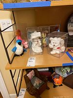 View of several Beanie Babies including a blue bird (Rocket), a pink flamingo, a white bear (Valentino), and others inside acrylic display cases on a shelf.
