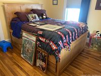 Full view of queen storage bed with headboard, bedding, and framed artwork on mattress
