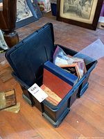 Plastic tote on floor filled with vintage books with visible red and blue covers, some packed with plastic bags inside tote.