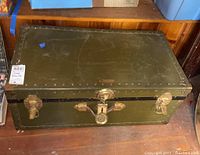 Photo of green metal camp trunk closed, showing top and brass hardware.