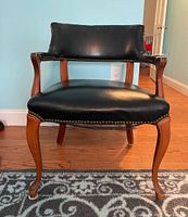 Front view showing black leather-like upholstered backrest and seat with brass upholstery tacks and curved wooden frame.