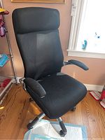 Front angle view of the black fabric upholstered office chair showing padded seat, backrest with headrest, and armrests on a wheeled base.
