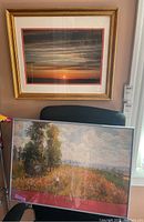 Framed sunset photo above framed Claude Monet exhibition poster leaning on chair.