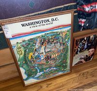 Photo of two different sized framed posters featuring a colorful illustrated map of Washington, D.C. placed on the floor next to each other.