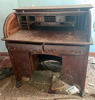 Front view of antique wooden rolltop desk showing drawers, desk surface, and rolltop section open exposing pigeonholes and small drawers.
