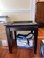Front view of the black wooden side table showing the tray top and four legs.