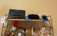 Image of Sony headphones, charging dock, blue carrying case, and Altec Lansing InMotion speaker on wooden shelf with figurines below