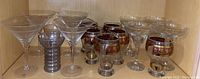 Wide view of the stemware set including martini glasses, decorative glasses with gold and red grapevine patterns, and other clear glasses