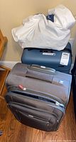Two suitcases stacked: blue hard shell suitcase on bottom with white protective cloth bag on top, black softside suitcase standing in front.