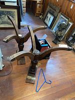 Two wooden table bases on a wood floor with various framing and household items in background.