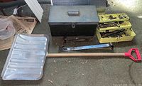 Full view of two toolboxes - one black closed and one yellow open showing assorted hand tools, plus metal snow shovel laid out on the ground