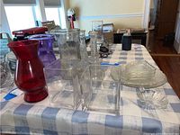 Various glass items on a checked tablecloth including colored vases, clear square vases, plates, and small dishes.