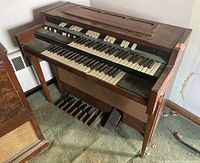 Full view of Hammond L-102 organ showing wooden body, dual keyboards, side panels, and pedals.