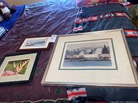 Three framed art pieces on a bed: butterfly photograph on left, smaller marina print at top left, and large coastal print at center