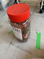 Photo of a clear 7-inch jar with a red lid, filled with US pennies, showing label indicating 'pennies 1 jar 7in jar'.