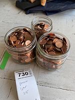 Three jars filled with copper-colored US pennies arranged closely on a light grey tiled floor.