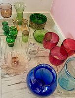 Full lot view showing diverse coloured glassware including pink, green, blue, red, and amber hues.