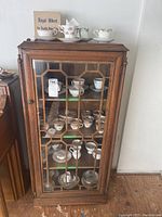 Front view of wooden display cabinet showing glass door with geometric mullions and contents
