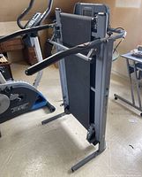 Folding Exerpeutic treadmill seen standing upright folded for storage, showing handles and control console.