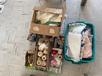 Overview of boxes and plastic bin with fabric pieces, thread spools, and sewing notions on floor
