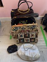 Six handbags and clutches arranged on the floor with clear visibility of design and color for each item