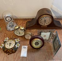 Overview of all clocks, barometers, thermometer, and framed clock on wooden floor