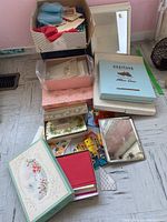 Overview of boxes, mirrors, vintage handkerchiefs, and stationery stacked on floor.