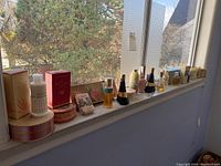 Overview of the lot showing various vintage perfume bottles, boxes and decorative tins arranged on a windowsill with outdoor background